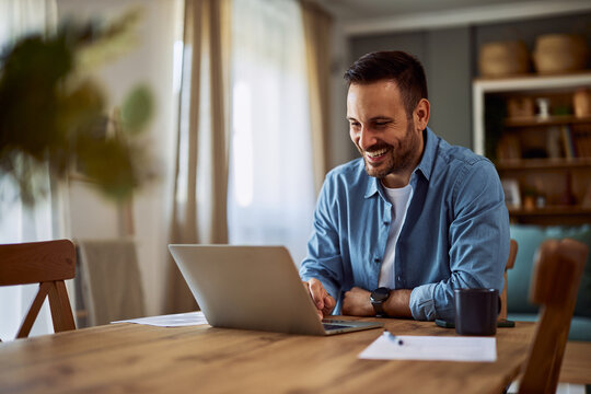 A happy adult freelance man on a video call with a client to overlook a project using his laptop at a desk.