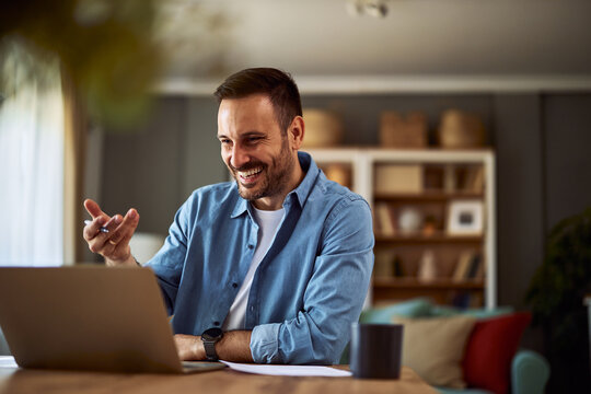 A cheerful adult male online teacher talking with his students on an online platform for his online class on his laptop.