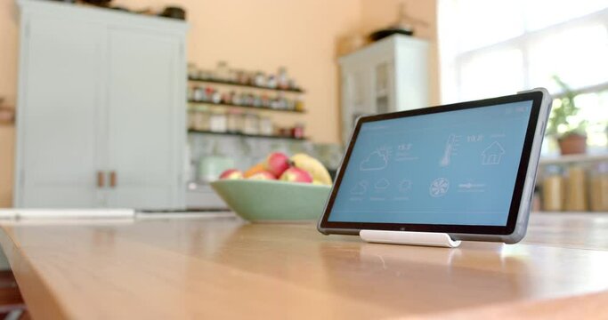 Close up of tablet with smart home on screen over fruit in bowl in kitchen, slow motion
