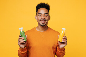 Young smiling fun man wear casual clothes hold show fruit juice green vegetable smoothie as detox diet isolated on plain yellow background. Proper nutrition healthy fast food unhealthy choice concept. - obrazy, fototapety, plakaty
