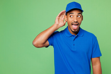 Professional delivery guy employee man wears blue cap t-shirt uniform workwear work as dealer courier try to hear you overhear listening intently isolated on plain green background. Service concept.