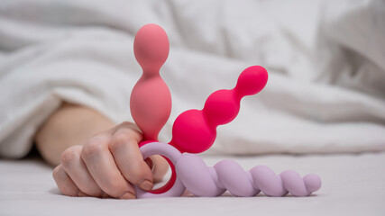 Woman holding three different anal beads while lying in bed. 