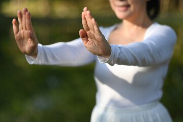 Smiling senior woman in white clothing practicing Tai Chi in the park. Health care concept