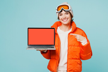 Skier young IT woman in padded windbreaker jacket hat ski goggles mask work use blank screen laptop...