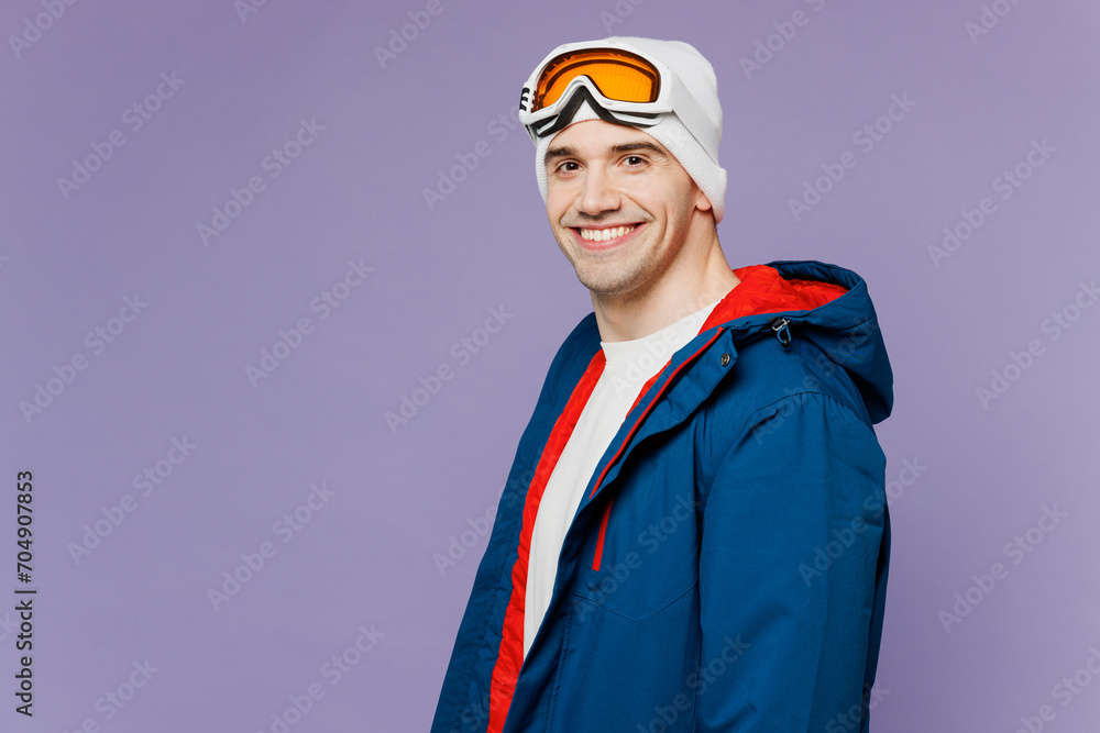 Wall mural Side view smiling happy skier man wears warm blue windbreaker jacket ski goggles mask look camera spend extreme weekend winter season in mountains isolated on plain purple background. Hobby concept.