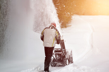 A man clears the snow from the street with a powerful snowblower after a heavy winter storm. Using...