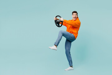 Full bodyside view young man wear orange hoody casual clothes hold steering wheel driving car raise up leg isolated on plain pastel light blue cyan color background studio portrait. Lifestyle concept