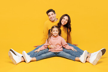 Full body young parents mom dad with child kid girl 7-8 years old wear pink sweater casual clothes sitting with outstretched legs posing kidding isolated on plain yellow background Family day concept - Powered by Adobe