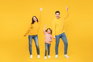 Full body young cool parents mom dad with child kid girl 7-8 years old wear pink sweater casual clothes do winner gesture dance point finger up isolated on plain yellow background. Family day concept.