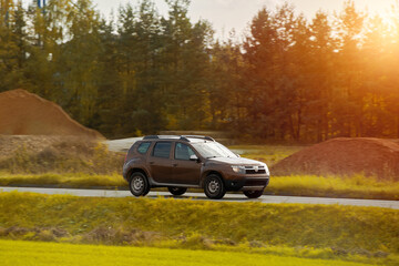 A subcompact SUV car explores the scenic countryside with a stunning sunset and alpine mountains in...