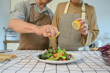 Cropped shot of senior couple squeezing fresh lemon juice into bowl with vegetable salad