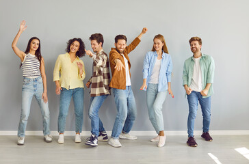 Obraz premium Portrait of a group of young happy smiling friends students or colleagues in casual clothes standing together, looking positively at the camera and having fun on a grey background.