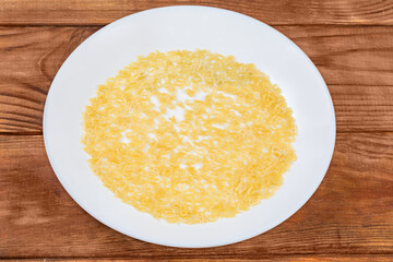 Raw alphabet pasta on dish on rustic table, top view