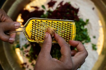 Grating ginger root with a grater in the kitchen, Grating ginger into shredded pieces, Close-up of hands with to shred ginger into a white plate,.