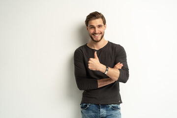 Portrait of cheerful man in casual clothing smiling and showing thumbs up at camera isolated over white