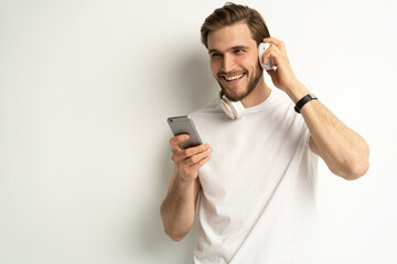 Caucasian young student man freelancer listening to the music in headphones, choosing sound track, song, playlist, podcast on phone isolated in white background.