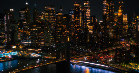Aerial Helicopter Cinematic Night Scene with Top Down View of the Brooklyn Bridge Switching to a Panoramic Shot with Skyscrapers Cityscape. Beautiful Office Buildings with Lights in the Dark