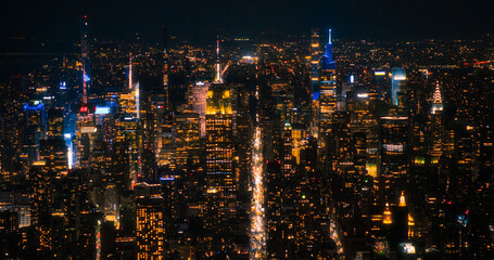 Fototapeta premium Aerial Night View of New York City Avenues in Manhattan, Business and Residential Building Roofs, Cars and Commercial Vehicles Driving at Night. Helicopter View a Straight Roads with Traffic
