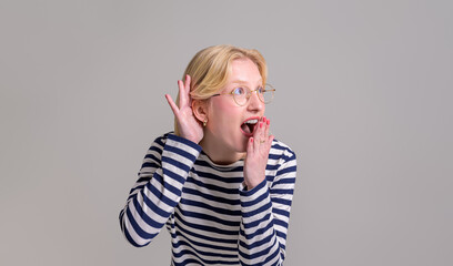 Excited shocked young woman covering her mouth with hand while listening gossip on white background
