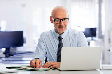 Mid aged businessman sitting in the office and having web conference