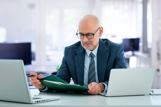 A middle-aged businessman sitting at his desk in the office and using a laptop for work