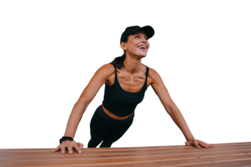 Tanned cheerful hispanic young woman doing pushups against transparent background on bench smiles looks away. Healthy lifestyle, sport. Amazed female runner preparing for marathon