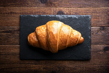 Freshly baked croissant on a black slate board on a naturally aged wooden table. Food photography