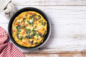 Italian Frittata made with spinach, tomatoes, onion and peppers on white wooden table. Top view. copy space