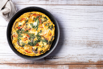 Italian Frittata made with spinach, tomatoes, onion and peppers on white wooden table. Top view. copy space