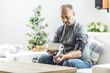 A mature man checking his blood pressure with a digital blood pressure monitor at home