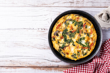 Italian Frittata made with spinach, tomatoes, onion and peppers on white wooden table. Top view. copy space
