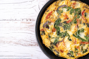 Italian Frittata made with spinach, tomatoes, onion and peppers on white wooden table. Top view. copy space