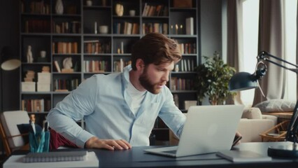 young man with beard in blue shirt sits at table in home office with feet on desk sleeping. wakes up in panic, checks time, takes clothes, hurry to quit and run away being late