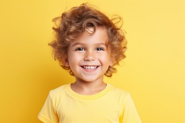 Portrait of a smiling little boy with curly hair over yellow background