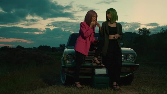 Two young women with colored hair smoking in front of the retro car
