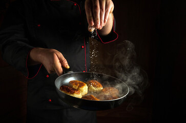 A professional chef salts hot pancakes in a frying pan while frying. The concept of making pancakes in the kitchen of a restaurant or hotel. Dark space for advertising.