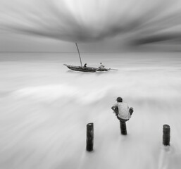 Not yet ready for the storm - preparations for the storm of fishermen on the old traditional sailer boat and the young boy is watching from the pier. Long exposure black and white photo.