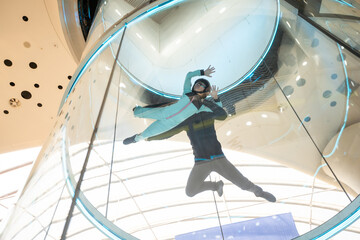 Excited teenage girl in helmet flying in aerodynamic tube wind tunnel. Skydiving training.
