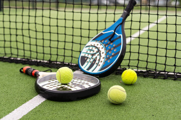 Blue padel racket and yellow balls placed on court near net on sunny day