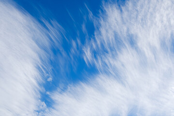 A serene skyscape featuring delicate, feathery cirrus clouds strewn across a clear blue sky,...