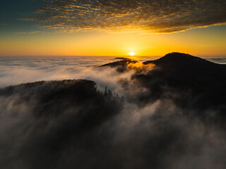 Fototapeta na wymiar Mountains in low clouds at sunrise. Aerial view of beautiful landscape of mountain peak in fog.