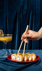 Sushi on a red plate on a blue velvet background, female hand taking sushi roll with chopsticks, close-up