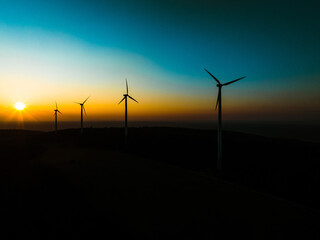 Aerial landscape photography of sunrise over nature with wind turbines. Windmill in soft morning light with forest, trees around. Concept of wind power as clean, renewable energy source.
