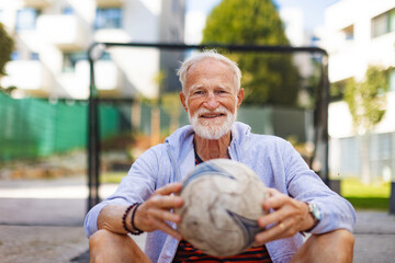 Senior man holding football in hands. Older, vital man has active lifestyle, doing sport every day.