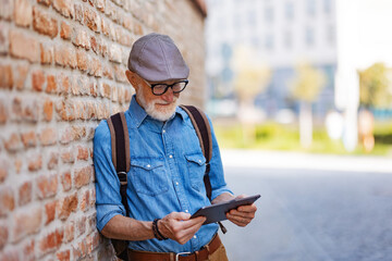 Senior tourist exploring new city, interesting places. Elderly man holding tablet and looking for the route. Traveling and solo trips in retirement.