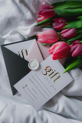 a beautiful spring bouquet of pink-red tulips lies on the bed with a gift certificate for a beauty procedure in an envelope, a gift for a woman for the holiday