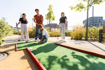 Group of smiling friends enjoying together playing mini golf in the city. - Powered by Adobe