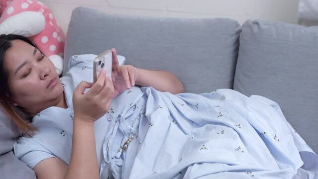 Woman lying down on a couch while she is browsing her phone to check her messages on her social media.