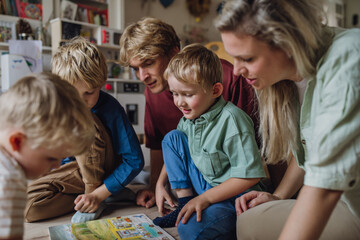 Cheerful family with three kids reading book in living room, on floor.