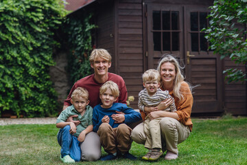 Portrait of family sitting in the garden on grass. Beautiful mother with her three sons and husband in the living room.